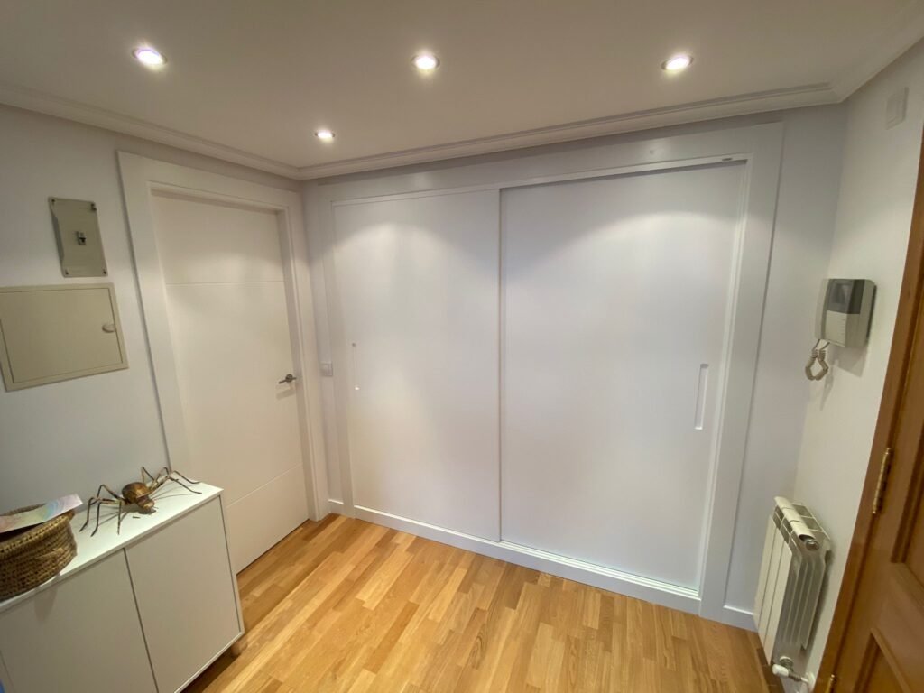 Pasillo moderno con suelo de madera y armario blanco.