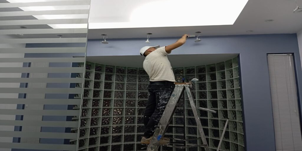 Hombre pintando techo sobre escalera en oficina moderna.