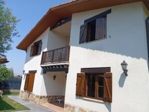 Casa campestre blanca con balcón y persianas de madera.