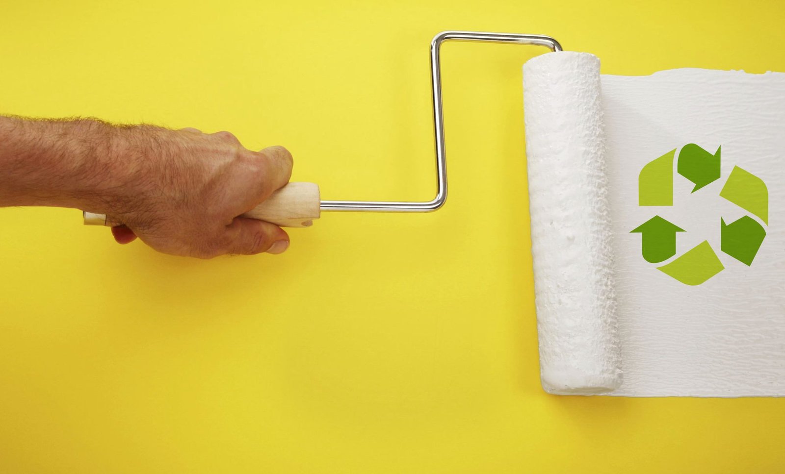 Rodillo pintando símbolo de reciclaje sobre fondo amarillo.